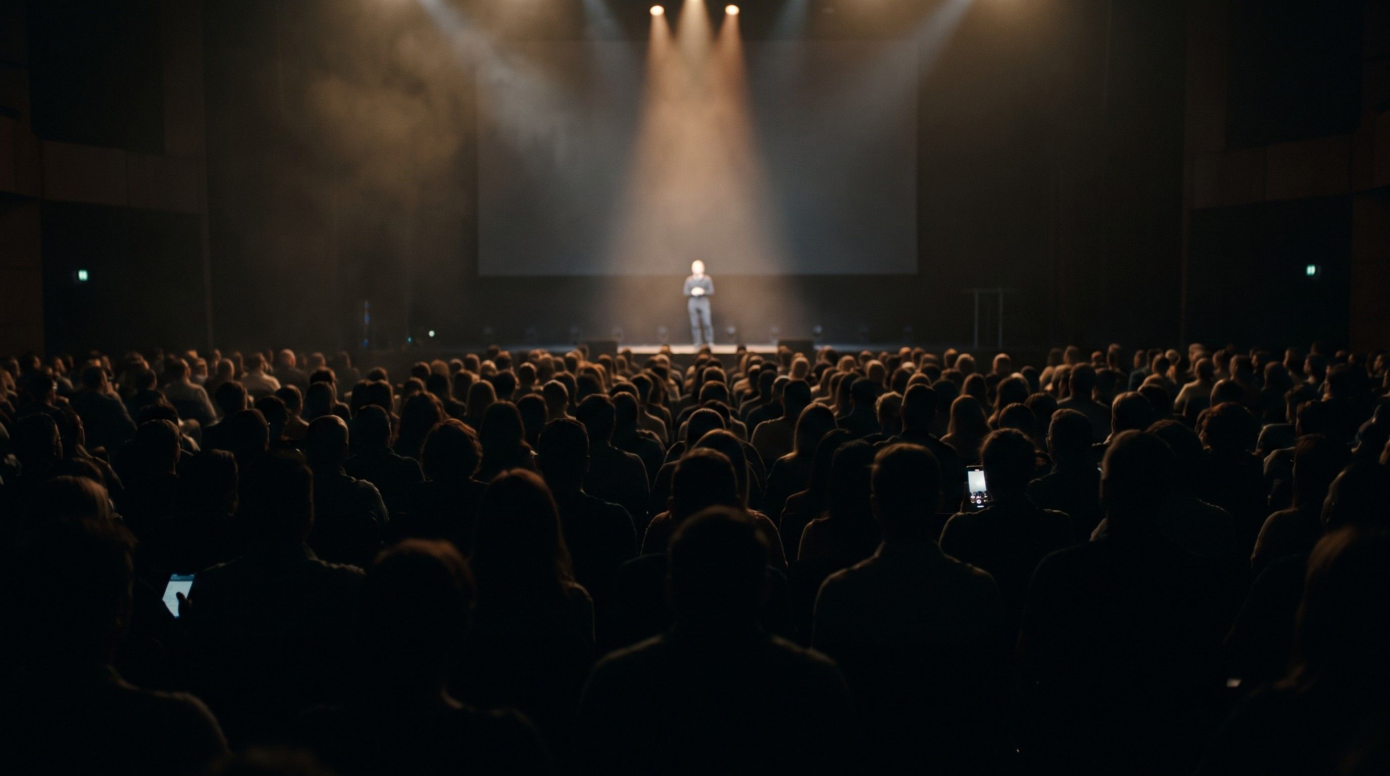 A keynote speaker in a spotlight seen over a dark audience